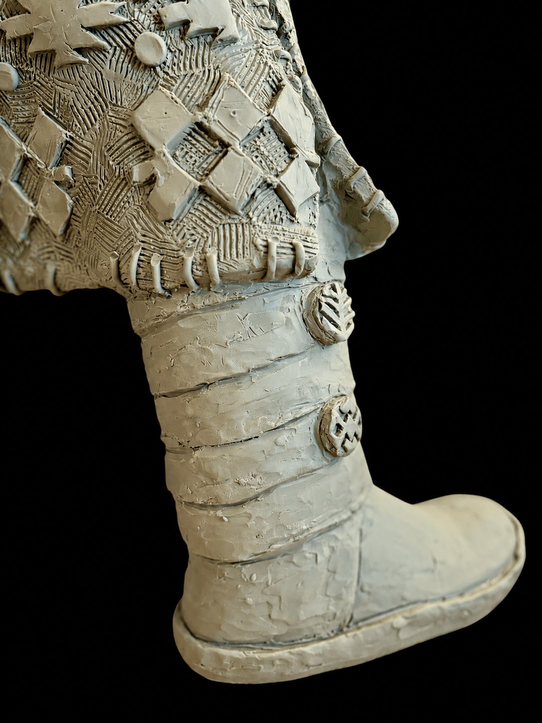 Close view of Ascending Girl’s sculpted clothing and moccasin against a black background.